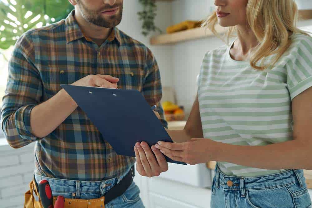 exclusive1 A man holding a clipboard explains something to a woman in a kitchen. The man wears a tool belt and plaid shirt; the woman, in jeans and a striped shirt, holds an Eastern Shore Spotlight postcard highlighting local print marketing reaching residents in Daphne.