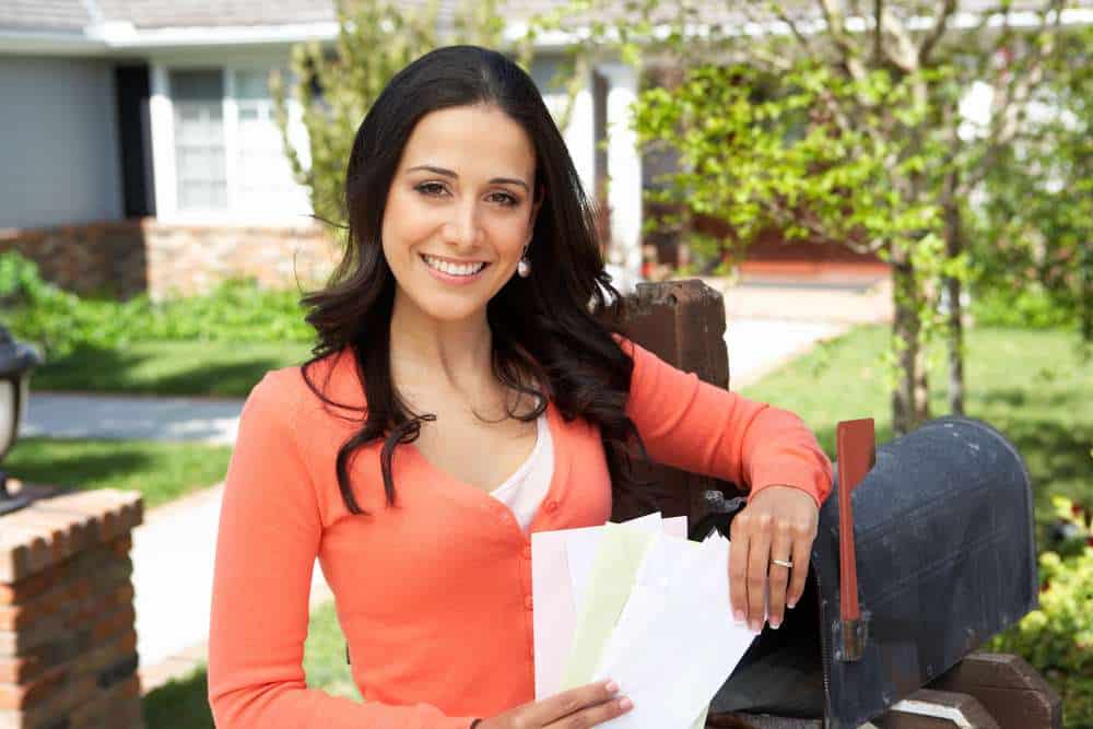 mail2 Woman holding an Eastern Shore Spotlight postcard stands by an open mailbox, smiling at the camera with a stack of envelopes—print marketing reaching residents in Daphne and supporting Fairhope small business growth.